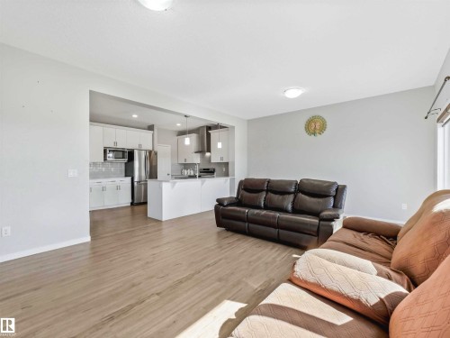 Open-concept living area with wood-finish flooring, recessed lighting, and a kitchen featuring white cabinetry and stainless steel appliances - 2435 12 Avenue Nw, Edmonton, AB 