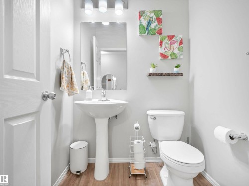 Pedestal sink with chrome faucet, wall-mounted mirror, and wood-finish flooring - 2435 12 Avenue Nw, Edmonton, AB 