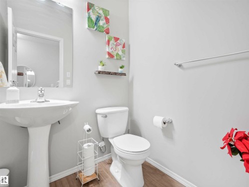 Pedestal sink with chrome faucet, toilet, wall-mounted mirror, and wood-finish flooring - 2435 12 Avenue Nw, Edmonton, AB 