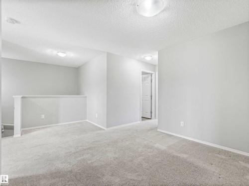 Carpeted upper level with painted walls and ceiling, featuring a partial wall railing and flush-mount lighting fixtures - 2435 12 Avenue Nw, Edmonton, AB 