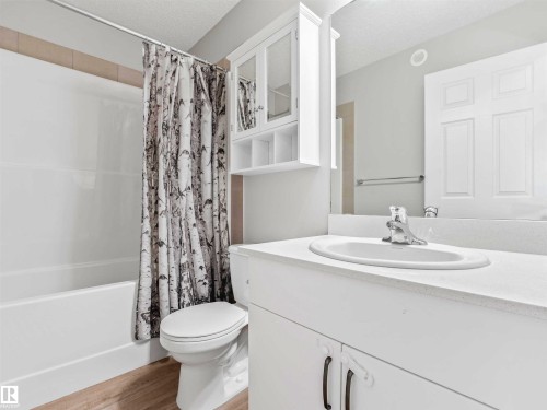 Bathroom featuring a white vanity with integrated sink, chrome faucet, and wood-finish flooring - 2435 12 Avenue Nw, Edmonton, AB 