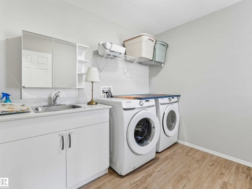Laundry space featuring a utility sink, white base cabinetry with dual handles, a medicine cabinet with open shelving, wood-finish flooring, and a wall-mounted wire shelf - 2435 12 Avenue Nw, Edmonton, AB 