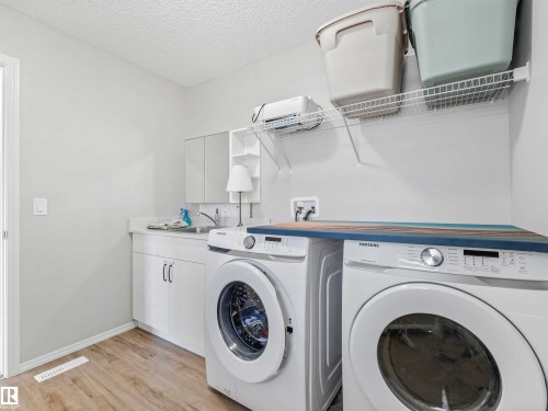 Laundry area featuring wood-finish flooring, white cabinetry, a built-in sink, and wire shelving - 2435 12 Avenue Nw, Edmonton, AB 