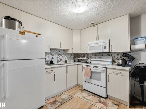 Compact kitchen featuring white cabinetry, a built-in microwave, white appliances, and a patterned tile backsplash - 2435 12 Avenue Nw, Edmonton, AB 