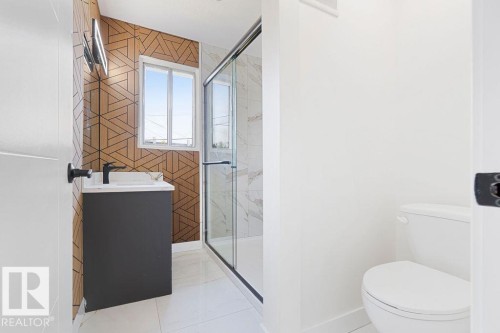 Contemporary bathroom featuring a geometric wood-finish accent wall, dark vanity with white countertop, and a glass-enclosed shower with tiled walls - 12303 131 St Nw Nw, Edmonton, AB 