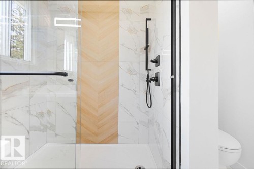 Glass-enclosed shower featuring a matte black shower system, white tile walls with veining, a wood-finish accent wall in a chevron pattern, and a white shower pan - 12303 131 St Nw Nw, Edmonton, AB 