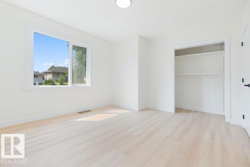 Light wood-finish flooring, built-in closet shelving, white interior door with black hardware, and a single window with white trim - 12303 131 St Nw Nw, Edmonton, AB 