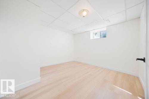 Light wood-finish flooring with white walls, a drop ceiling, and a single window - 12303 131 St Nw Nw, Edmonton, AB 