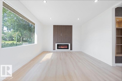 Spacious room featuring a wide window, light wood-finish flooring, a contemporary electric fireplace with a patterned accent wall, recessed lighting, and built-in shelving with integrated illumination - 12303 131 St Nw Nw, Edmonton, AB 