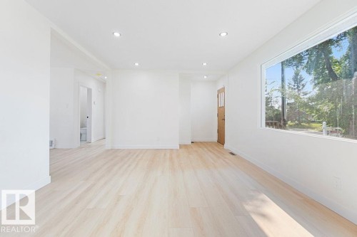 Expansive living space featuring light wood-finish flooring, recessed lighting, a large window, and crisp white walls - 12303 131 St Nw Nw, Edmonton, AB 