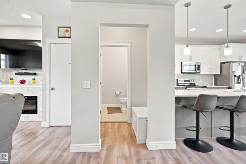 Wood-finish flooring throughout, bright white kitchen cabinetry, stainless steel appliances, and a white marble-look fireplace surround - 8024 Orchards Green Green Sw, Edmonton, AB 