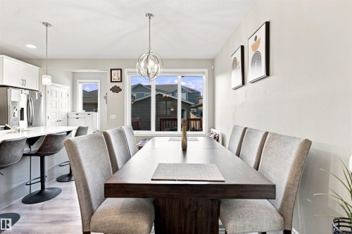 Open-concept dining area featuring a contemporary chandelier, large windows, and light wood-finish flooring - 8024 Orchards Green Green Sw, Edmonton, AB 