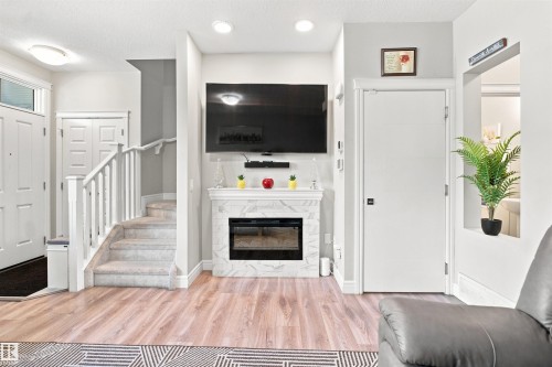 Laminate wood-finish flooring, built-in fireplace with a stone-finish mantel, white paneled doors, and a carpeted staircase with white railings - 8024 Orchards Green Green Sw, Edmonton, AB 