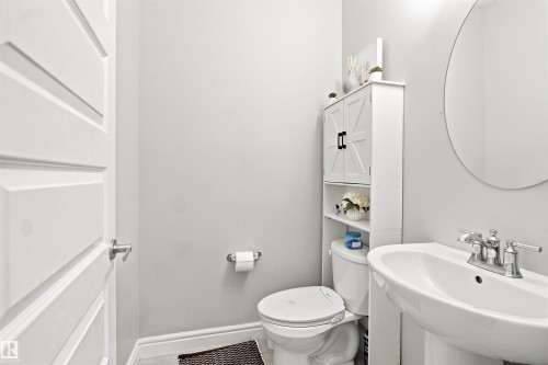 Pedestal sink with chrome faucet, circular wall mirror, and white panel door - 8024 Orchards Green Green Sw, Edmonton, AB 