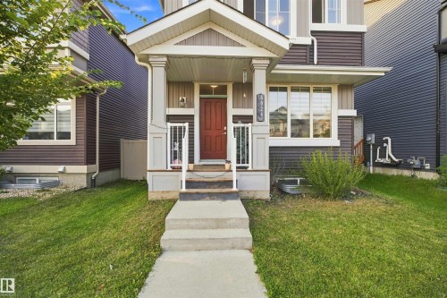 Covered front entry with a red door, white trim, and a concrete pathway - 8024 Orchards Green Green Sw, Edmonton, AB 