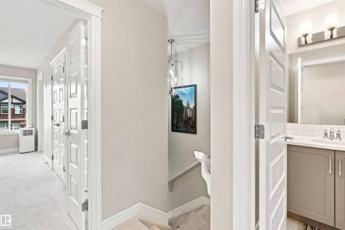 Hallway featuring light-colored carpeting, white paneled doors, and a window with trim - 8024 Orchards Green Green Sw, Edmonton, AB 
