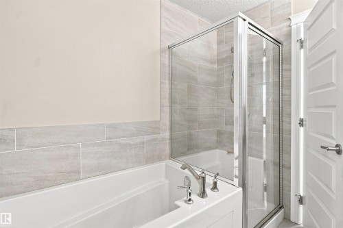Bathtub with chrome fixtures, glass-enclosed shower, and light-toned tile surround - 8024 Orchards Green Green Sw, Edmonton, AB 