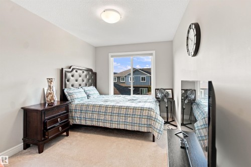 Light-toned wall paint, large window with white trim, upholstered headboard, flush-mount ceiling light fixture, and neutral carpeting - 8024 Orchards Green Green Sw, Edmonton, AB 