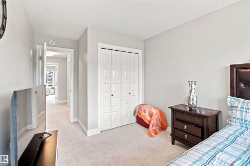 Soft gray wall paint, light-colored carpeting, white paneled bifold closet doors, white trim, and a dark wood-finish nightstand - 8024 Orchards Green Green Sw, Edmonton, AB 