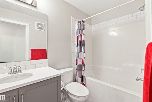 Bathroom with a vanity featuring a white countertop and gray cabinetry, subway tile backsplash, and a white bathtub with a shower and white subway tile accent - 8024 Orchards Green Green Sw, Edmonton, AB 