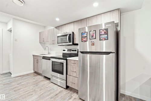 Kitchen featuring wood-finish cabinetry, stainless steel appliances, white countertops, and wood-finish flooring - 8024 Orchards Green Green Sw, Edmonton, AB 