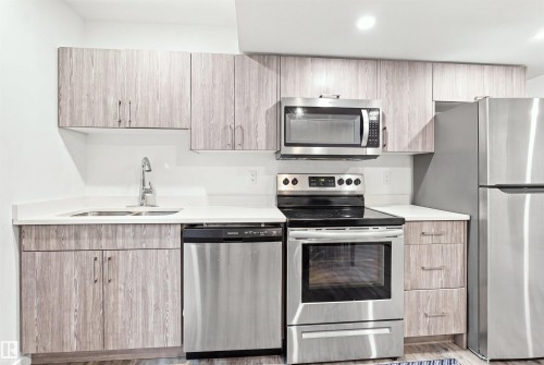 Kitchen featuring wood-finish cabinetry, stainless steel appliances, a double basin sink, and a white countertop - 8024 Orchards Green Green Sw, Edmonton, AB 