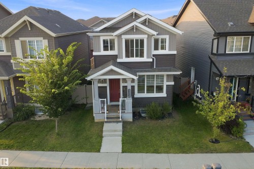 Two-story exterior with a contrasting facade, covered front porch, front yard landscaping, and an integrated garage - 8024 Orchards Green Green Sw, Edmonton, AB 