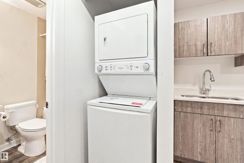 Stackable washer and dryer, wood-finish flooring, built-in cabinetry, stainless steel sink, and gooseneck faucet - 8024 Orchards Green Green Sw, Edmonton, AB 