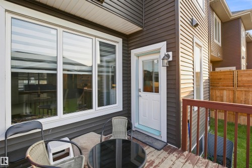 Ground-level deck with wood-finish railing, white exterior door, and adjacent large multi-pane window - 8024 Orchards Green Green Sw, Edmonton, AB 