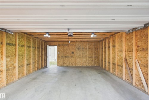 Attached garage featuring a concrete floor, exposed wood-frame walls, and overhead lighting fixtures - 8024 Orchards Green Green Sw, Edmonton, AB 