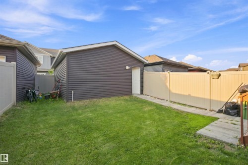 Manicured lawn with a detached building featuring dark siding and a white entry door - 8024 Orchards Green Green Sw, Edmonton, AB 