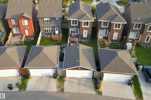 Gable roofline, attached garage with white door, concrete driveway, and green lawn areas - 8024 Orchards Green Green Sw, Edmonton, AB 