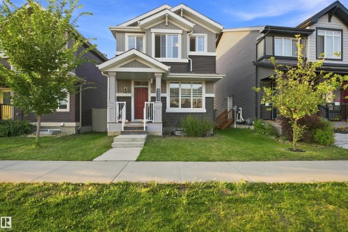 Two-story residential exterior featuring a covered entry, dark siding, white trim, and multiple windows - 8024 Orchards Green Green Sw, Edmonton, AB 