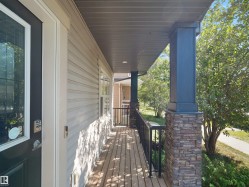 Covered porch with wood-finish decking, stone-clad support columns, and black metal railing - 