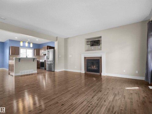 Hardwood-finish flooring throughout, featuring a gas fireplace with a white mantel, and an open-concept kitchen with a breakfast bar and stainless steel appliances - 5190 1B Avenue Sw, Edmonton, AB 