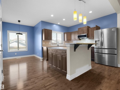Wood-finish flooring throughout, kitchen with wood cabinetry, stainless steel appliances, and an island with an extended countertop - 5190 1B Avenue Sw, Edmonton, AB 