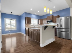 Wood-finish flooring throughout, kitchen with wood cabinetry, stainless steel appliances, and an island with an extended countertop - 
