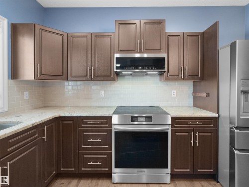 Kitchen featuring dark wood-finish cabinetry, light-colored countertops, subway tile backsplash, and stainless steel appliances - 5190 1B Avenue Sw, Edmonton, AB 