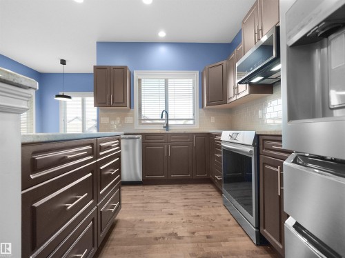 Kitchen featuring wood-finish flooring, dark wood cabinetry, stainless steel appliances, and a tile backsplash - 5190 1B Avenue Sw, Edmonton, AB 