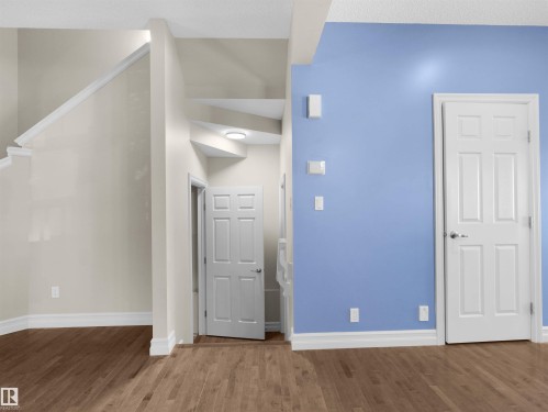 Wood-finish flooring, white trim, staircase with white railing, paneled interior doors, and a ceiling-mounted light fixture - 5190 1B Avenue Sw, Edmonton, AB 