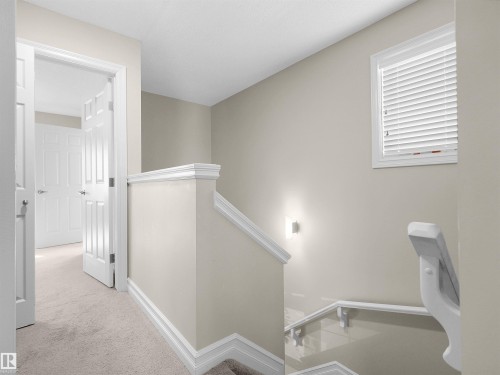 Hallway with neutral carpeting, white trim, and a window with blinds - 5190 1B Avenue Sw, Edmonton, AB 