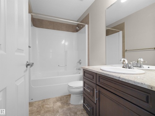 Bathroom featuring a dark wood-finish vanity with a light-toned countertop, an integrated sink, a large wall mirror, and a shower-tub combination with tile surround - 5190 1B Avenue Sw, Edmonton, AB 
