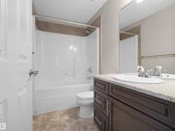 Bathroom featuring a dark wood-finish vanity with a light-toned countertop, an integrated sink, a large wall mirror, and a shower-tub combination with tile surround - 