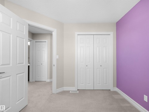 Neutral carpet flooring, white bi-fold closet doors, white paneled doors with brushed nickel hardware, and white trim molding - 5190 1B Avenue Sw, Edmonton, AB 