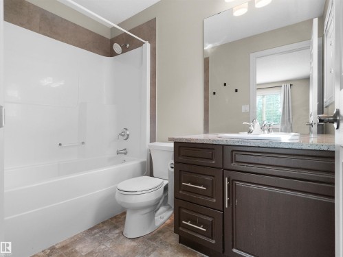 Full bathroom featuring a dark wood-finish vanity with a granite-style countertop, integrated sink, and an expansive wall mirror - 5190 1B Avenue Sw, Edmonton, AB 