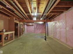 Unfinished basement with concrete flooring, exposed wood framing, and pink insulation - 