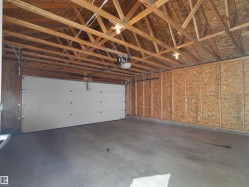 Garage interior featuring exposed ceiling trusses, concrete flooring, and a sectional overhead door with an automatic opener - 