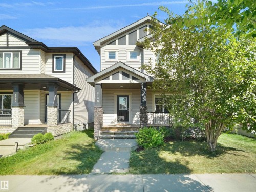 Two-story residence featuring light-colored siding, a covered porch with stone-clad columns, and a dark entry door - 5190 1B Avenue Sw, Edmonton, AB 