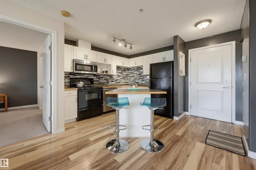 Open-concept kitchen featuring white cabinetry, black appliances, a tile backsplash, and a breakfast bar with wood-finish countertop - #314 245 Edwards Dr Sw, Edmonton, AB - Indoor Photo Showing Kitchen