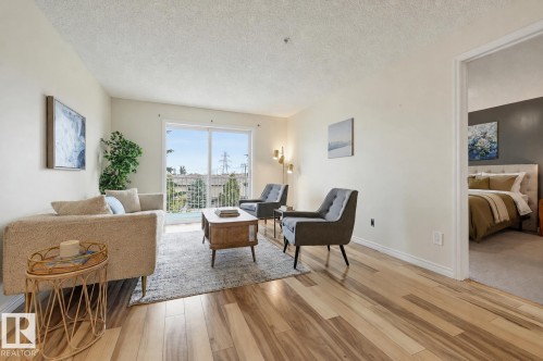 Open living area featuring wood-finish flooring and a sliding glass door to a balcony - #314 245 Edwards Dr Sw, Edmonton, AB - Indoor Photo Showing Living Room
